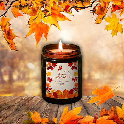 Płonąca świeca sojowa Pumpkin Spice w brązowym słoiczku z etykietą „Hello Autumn”, wśród jesiennych liści na drewnianym stole