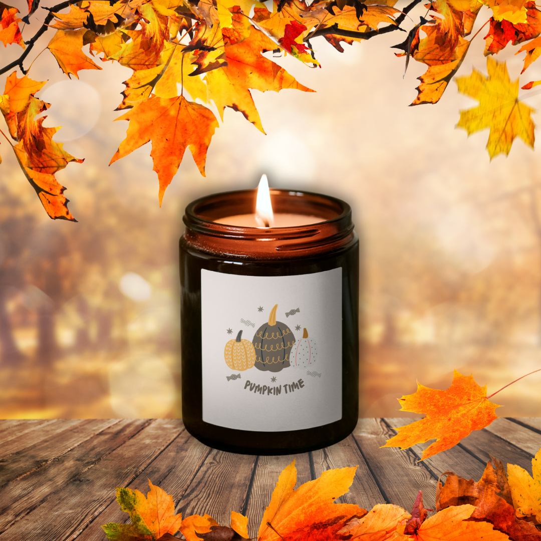 Płonąca świeca sojowa Pumpkin Spice w brązowym słoiczku z etykietą „Pumpkin time”, wśród jesiennych liści na drewnianym stole