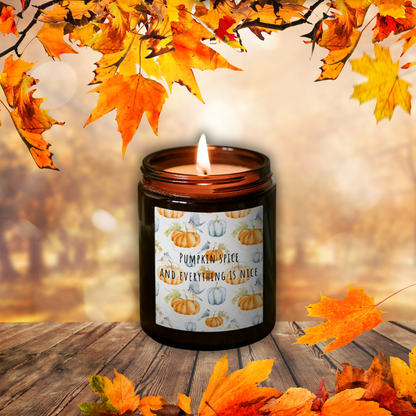 Płonąca świeca sojowa Pumpkin Spice w brązowym słoiczku z etykietą „Pumpkin spice and everything is nice”, wśród jesiennych liści na drewnianym stole