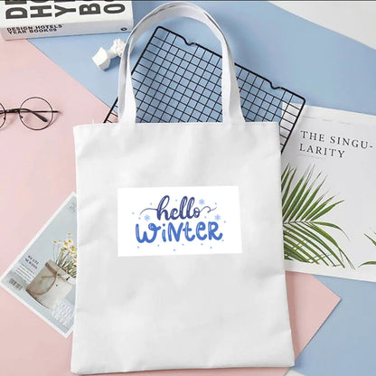 Torba płócienna Kiskedves Hello Winter w kolorze białym, z niebieskim napisem hello winter, na pastelowym tle obok magazynów i okularów.