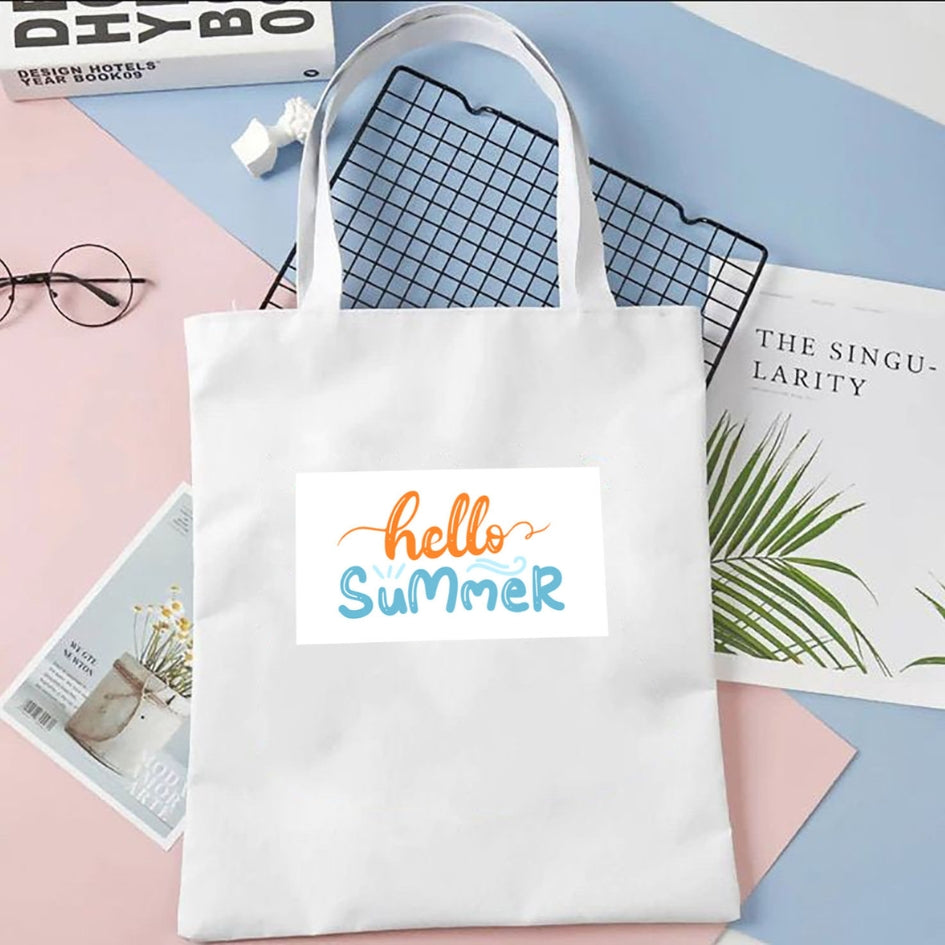 Torba płócienna Kiskedves Hello Summer w kolorze białym, z pomarańczowo-niebieskim napisem hello summer, na pastelowym tle obok magazynów.