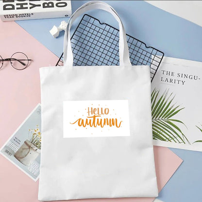 Torba płócienna Kiskedves Hello Autumn w kolorze białym, z pomarańczowym napisem hello autumn, na pastelowym tle obok magazynów.
