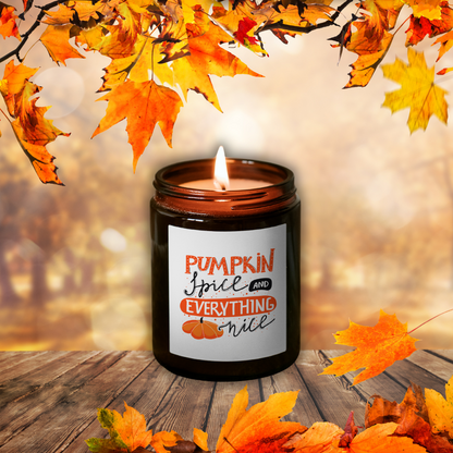 Płonąca świeca sojowa Pumpkin Spice w brązowym słoiczku z etykietą „Pumpkin Spice and everything nice”, wśród jesiennych liści na drewnianym stole