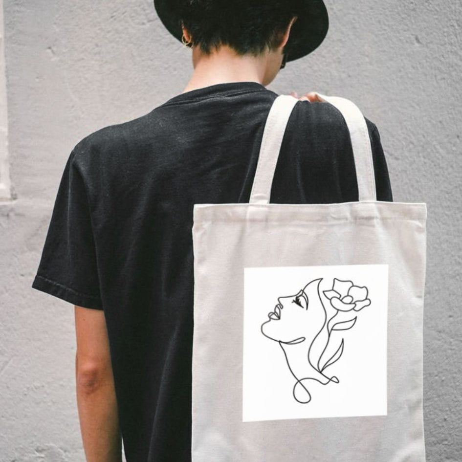Torba płócienna Kiskedves Line Art na plecach, twarz z kwiatem we włosach, na osobie w czarnej koszulce.