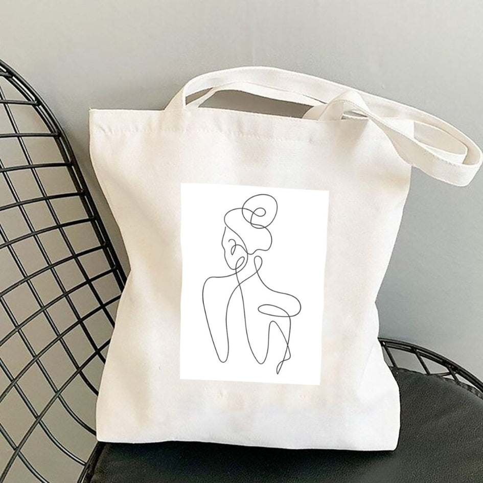 Torba płócienna Kiskedves Line Art z postacią od tyłu, na czarnym krześle z drutu.