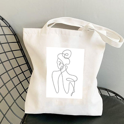 Torba płócienna Kiskedves Line Art z postacią od tyłu, na czarnym krześle z drutu.