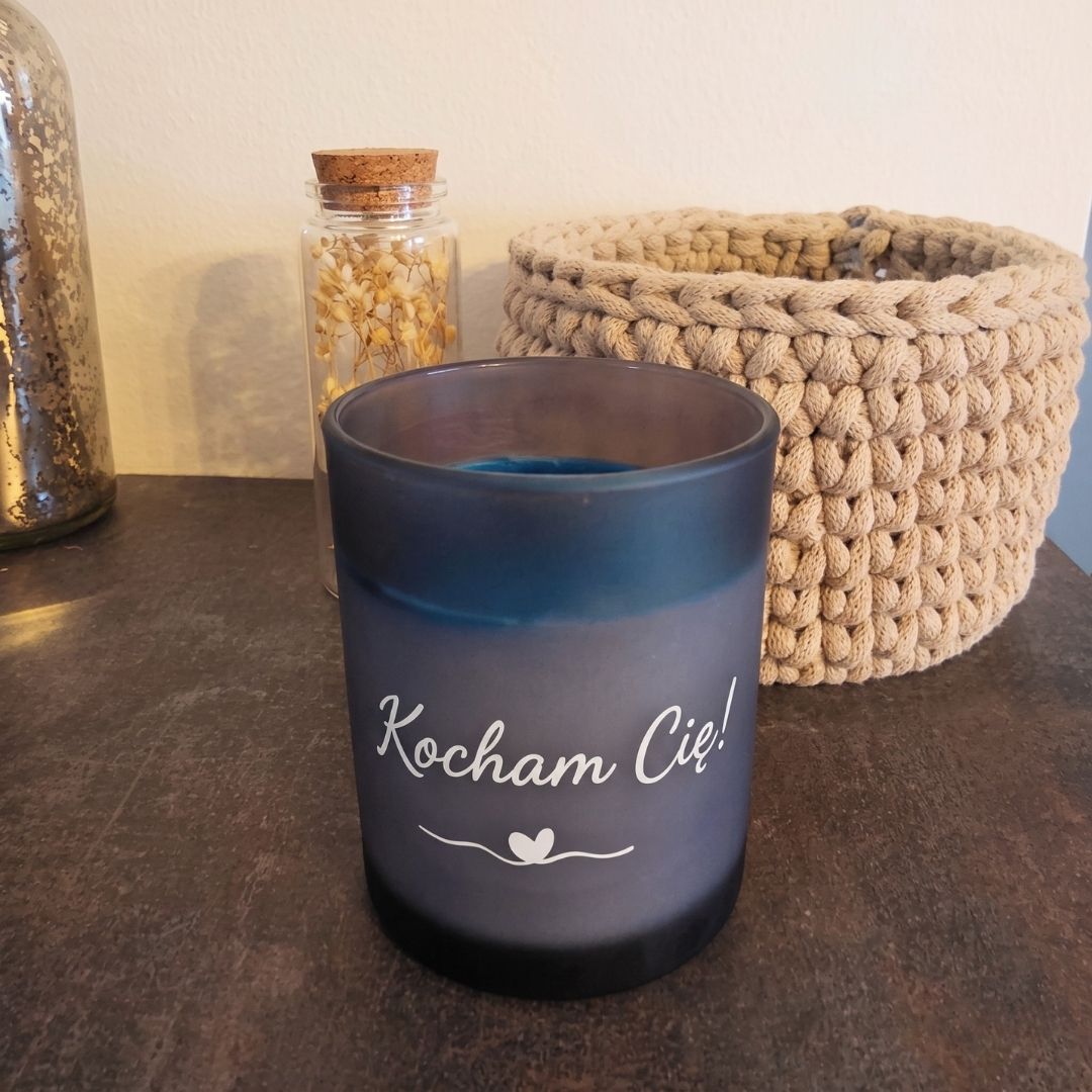 Ocean personalizowana świeca dekoracyjna bez pokrywki, z napisem „Kocham Cię”, obok szydełkowanego koszyka i buteleczki z suszonymi kwiatami