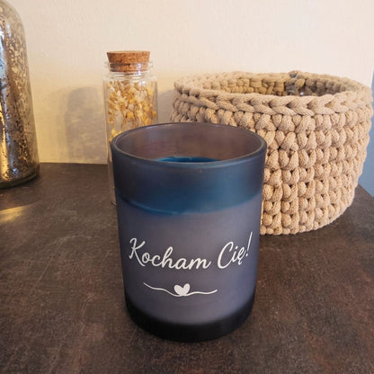 Ocean personalizowana świeca dekoracyjna bez pokrywki, z napisem „Kocham Cię”, obok szydełkowanego koszyka i buteleczki z suszonymi kwiatami