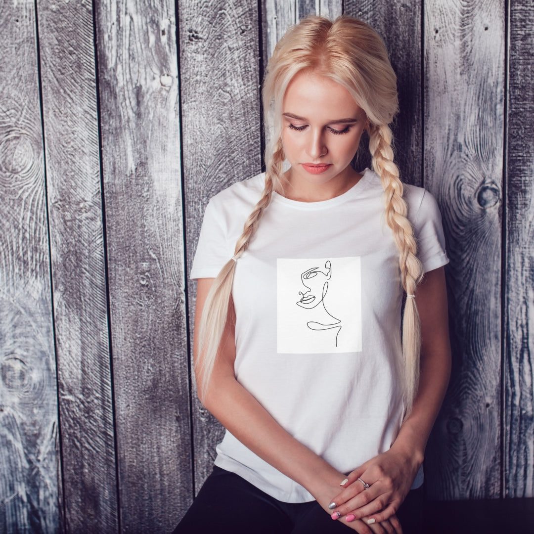 Biała koszulka Kiskedves Line Art z kobiecym profilem, na modelce z warkoczami przed drewnianą ścianą.