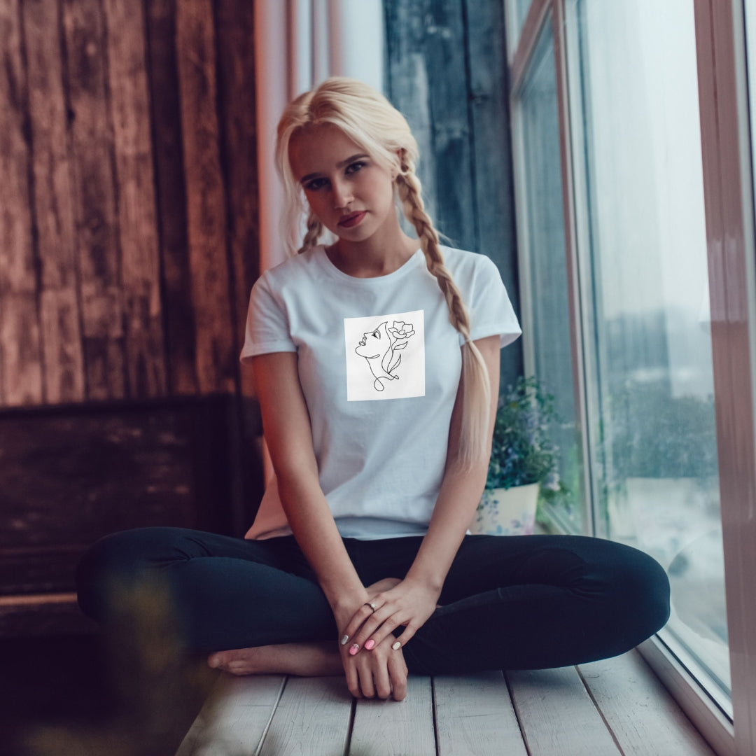 Biała koszulka Kiskedves Line Art z kwiatem we włosach, na siedzącej modelce przy oknie.
