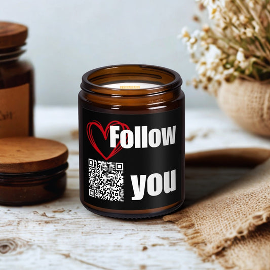 Świeca sojowa Kiskedves w brązowym szklanym słoiczku z drewnianym knotem, na etykiecie kod QR i piosenka Follow You, na drewnianym stole obok suszonych kwiatów