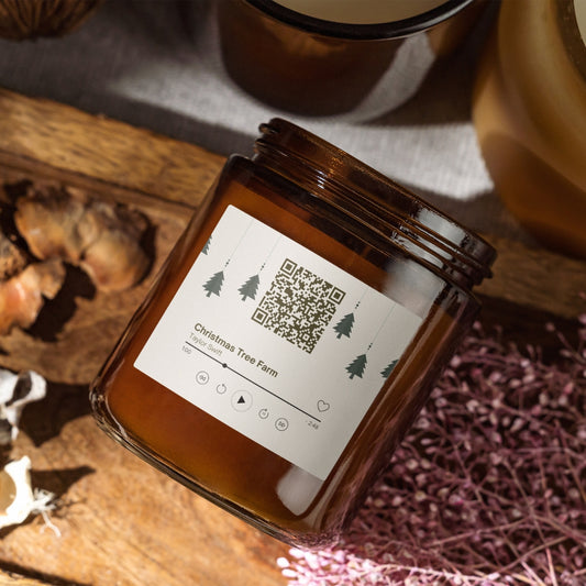 Świąteczna świeca „Melodyjna” Kiskedves w brązowym słoiczku, na etykiecie kod QR i karta odtwarzacza z piosenką Christmas Tree Farm
