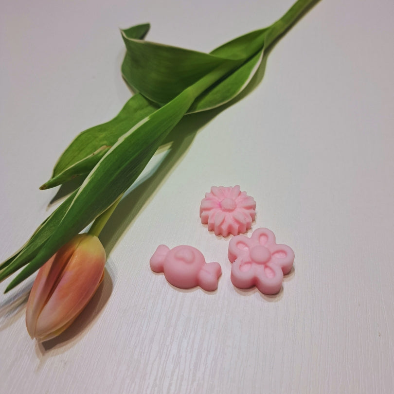 Wiosenny zestaw wosków zapachowych Kiskedves: różowy króliczek, margerytka i kwiat na białym drewnianym stole, obok tulipan.